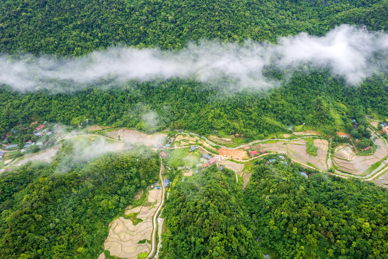 Aerial view of forested hills, terraced fields and village homes beneath low clouds.